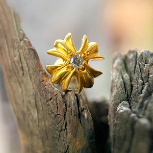 Detail view of a gold cross stud earring with a clear zircon stone on wood background
