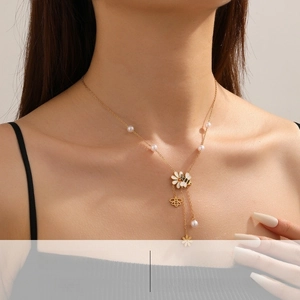 Dettaglio di collana a Y dorata con pendenti a margherita bianca e ape con perla