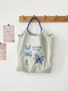 Detail of light green tote bag featuring butterfly embroidery and woven blue handles