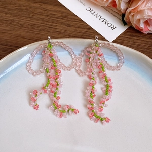 Detail shot of beaded pink and green bow tassel earrings on a white ceramic plate