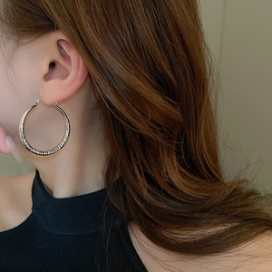 Close-up of a large gold hoop earring with textured stripe design on a female model