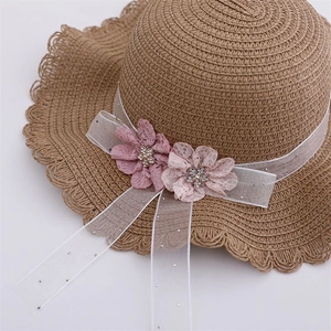 Détail du chapeau de paille enfant avec bord ondulé et fleurs en dentelle rose pailletées