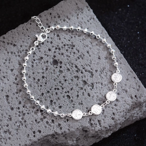 Minimalist silver beaded bracelet with engraved round lucky charms on a grey stone background