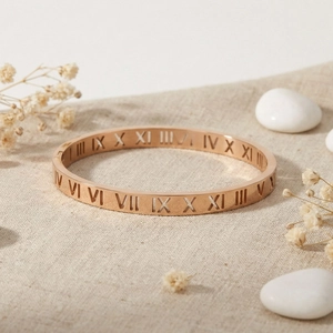 Close-up of rose gold stainless steel hollow Roman numeral bangle on natural linen texture