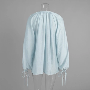 Detail of back view showing sheer pleated fabric and bow-tie cuffs on light blue V-neck blouse