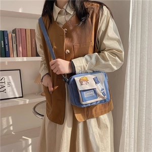 Close-up of a blue and beige canvas crossbody bag with cute cartoon patch on a shelf