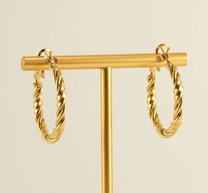 Close-up of golden twisted hoop earrings on a display stand with high polish finish