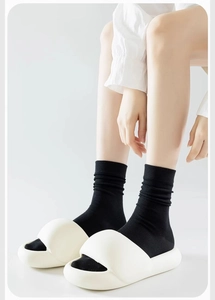 Close-up of black mid-calf cotton socks paired with white platform slides on a model