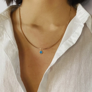 Minimalist gold titanium necklace featuring a blue round zircon pendant worn by a model