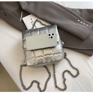 Top view of silver quilted square bag with chain strap next to a grey suit and smartphone