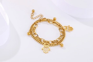 Detail of gold double-layer chain bracelet featuring Hamsa hand and polished bead pendants