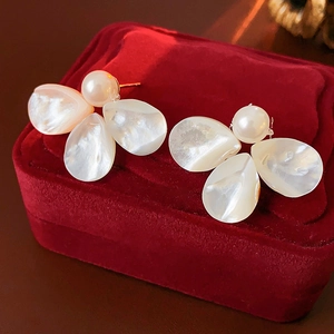 Detail of mother of pearl flower stud earrings with a gold metal frame on red velvet