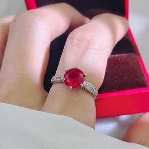 Macro detail of a 2-carat red ruby ring on a finger with pave diamond silver band