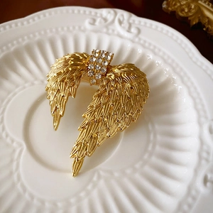 Gros plan d'une broche ailes dorées vintage avec strass brillants sur un plat en céramique