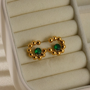 Macro view of gold plated C-shaped earrings featuring green stones in jewelry box