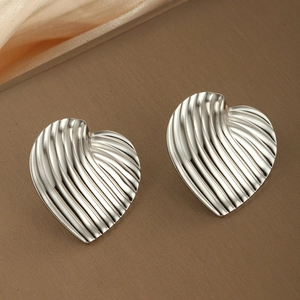 Boucles d'oreilles cœur en argent avec texture ondulée sur fond en tissu beige et marron
