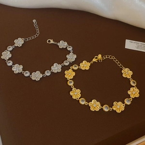 Détail de bracelets fleur or et argent avec zircons sur fond marron foncé élégant