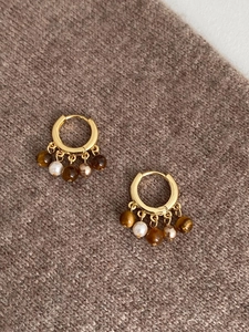 Détail des boucles d'oreilles en or 18k avec oeil de tigre et perles sur tissu marron