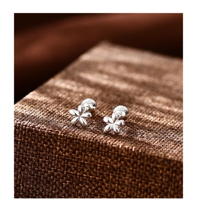 Vista macro de pendientes de flores en plata S999 con cierre de bola sobre fondo texturizado