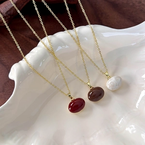 Elegant gold necklaces with red, brown, and ivory bean pendants on a white shell tray