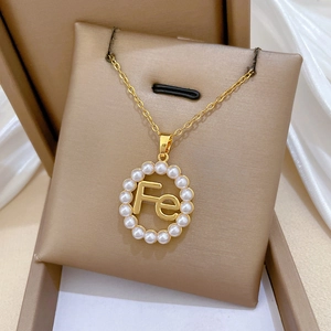 Macro shot of gold pendant with Fe initial and pearl halo resting on velvet padding