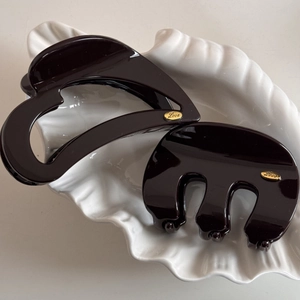 Detail of dark brown and black hair claws with gold Love tags in a shell tray