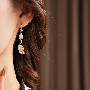 Close-up of a gold hollow butterfly earring with a zircon stud worn on a model's ear