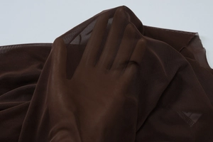 Close-up of sheer dark brown mesh fabric texture with hand showing material transparency
