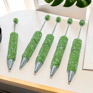 Set of five green rhinestone DIY beaded pens with silver tips on a white desk