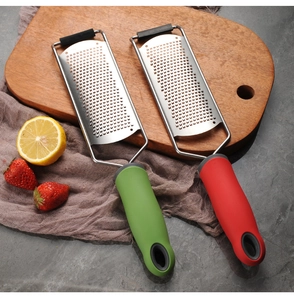Close-up of red and green handheld cheese graters on a wooden board with fresh fruits
