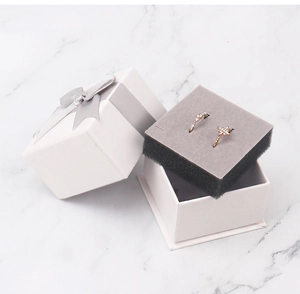 Detailed view of an open white jewelry box with a grey ribbon and two golden rings