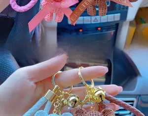 Close-up of bear keychain with knit texture, braided strap, and golden bell detail