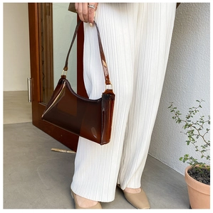 Detail of transparent brown PVC baguette bag with gold metal hardware held by a model