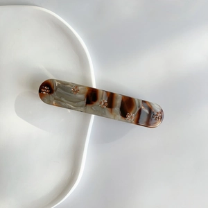 Detail view of marble-pattern hair clip with gold flower inlay on white ceramic plate