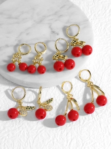 Macro detail of red cherry hoop earrings with gold hardware and sparkling zircons