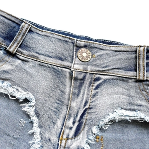 Dettaglio di pantaloncini in denim azzurro con bordi sfilacciati e bottone in ottone