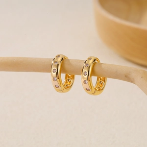 Fashionable gold-plated copper hoop earrings with cubic zirconia set on a natural wood branch