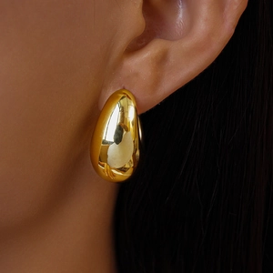 Close-up of a polished gold teardrop earring worn to show fit and metallic luster