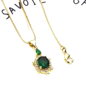 Detailed macro view of turtle pendant with green gemstone and cubic zirconia on gold chain