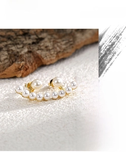 Detail of elegant curved pearl earrings with gold base on a textured natural background