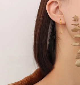 Close-up of golden twisted rope chain earrings worn by a model in a minimalist style