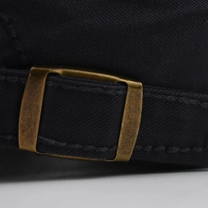 Detail of adjustable bronze metal buckle and stitching on black canvas peaked cap