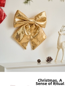 Sparkling gold sequined Christmas bow ornament hanging against a festive white wall decor