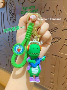 Detail of green dinosaur keychain with headphones and ukulele on a woven green lanyard