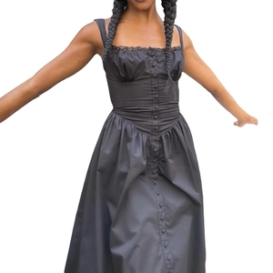 Détail d'une robe noire sans manches avec boutons sur le devant et ourlet plissé élégant