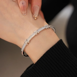 Close-up of a silver X-shaped buckle bracelet with micro-pave zirconia on a black sleeve