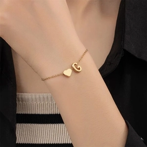 Detailed close-up of a gold heart and letter G pendant bracelet on a woman wrist