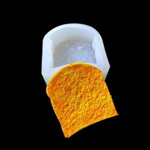 Detail of white silicone toast mold and a finished golden bread slice on black background