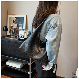 Close-up of the woven black leather tote bag worn by a model in a cozy home setting