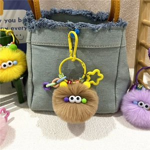 Detailed close-up of fluffy soot sprite keychain with colorful star clasp on denim bag
